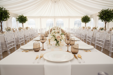 Load image into Gallery viewer, Elegant tablescape with gold-rimmed charger, brown Bibi glassware, Gems cutlery, and clear chiavari chairs
